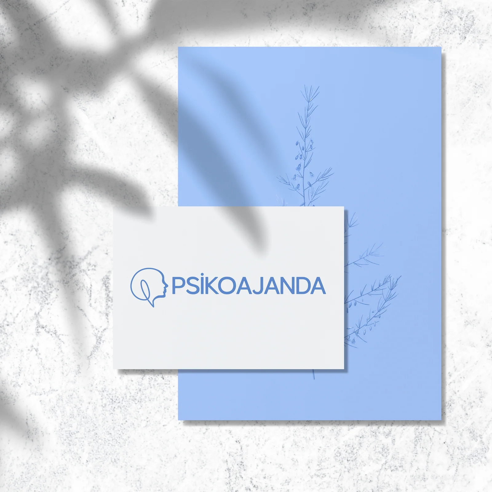 Psikoajanda brand presentation: a white card with the profile and speech-bubble mark over a blue botanical background.